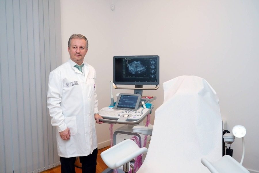 Il Dr. Athanasios Garavelas nella sala ecografica della clinica Ovagenesis, accanto a un macchinario per ecografie e una poltrona per visite ginecologiche