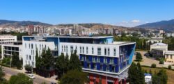 Vista esterna panoramica della LeaderMed Clinic a Tbilisi, Georgia: edificio moderno con facciata blu e bianca, finestre ampie, circondato da alberi verdi e skyline urbano con montagne innevate sullo sfondo sotto cielo azzurro sereno. Ideale per profili e SEO su cliniche IVF in Georgia.