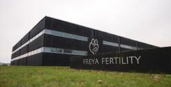 Vista esterna dell'edificio della clinica Freya Fertility. L'edificio è di colore nero con vetrate orizzontali. Davanti ad esso si trova il logo con la scritta “Freya Fertility”, circondato da un prato verde.