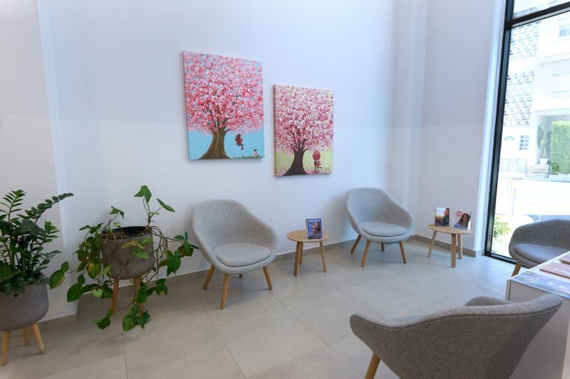 Moderna sala d'attesa della Cryos IVF Clinic Cyprus con sedie grigie, eleganti opere d'arte raffiguranti alberi di ciliegio in fiore, piante da interno e luce naturale, che riflettono un ambiente accogliente e tranquillo per i pazienti.