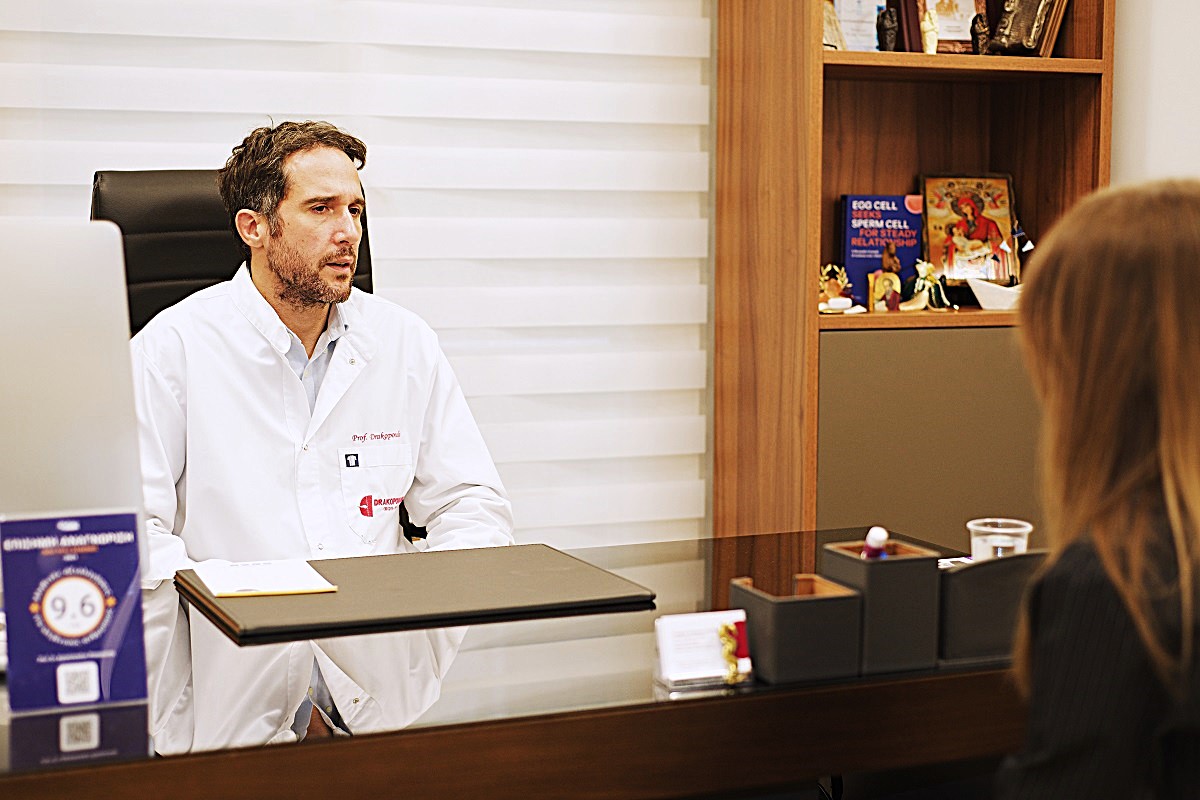 Il Prof. Dr. Panagiotis Drakopoulos visita una paziente nel suo studio. Sullo sfondo si vede una libreria.